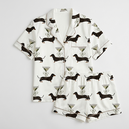 Women's satin pajama set with black dachshunds beside martini glasses tied with ribbon bows on white - flat lay