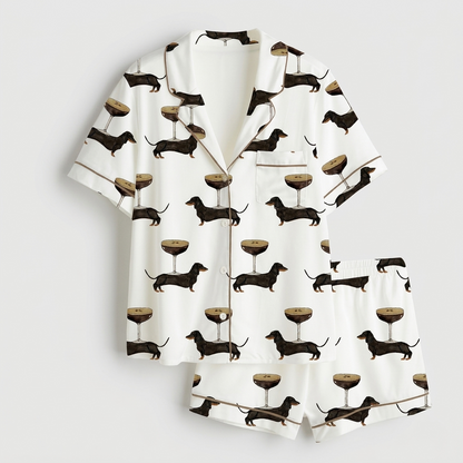 Women's satin pajama set with black dachshunds beside espresso martinis topped with coffee beans on white - flat lay