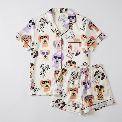 Women's satin pajama set with Labradors and dalmatians in bold sunglasses with confetti and party horns on white - flat lay