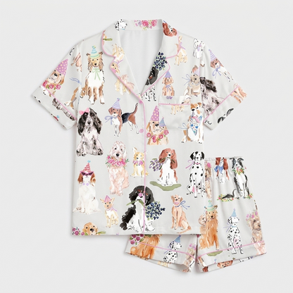 Women's satin pajama set with dogs in pastel party hats and flower crowns on soft gray - flat lay