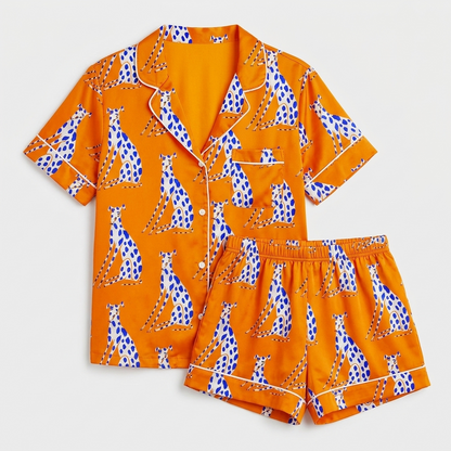 Women's satin pajama set with seated blue-spotted greyhounds on a bright tangerine orange background - flat lay