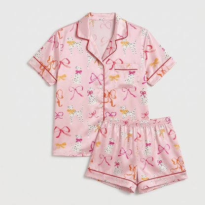 Women's satin pajama set with Dalmatians among scarlet, coral and gold ribbon bows on pink with red piping - flat lay