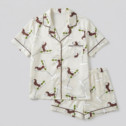 Women's satin pajama set with dachshunds stretched across martini glasses and olive picks on white with brown piping - flat lay