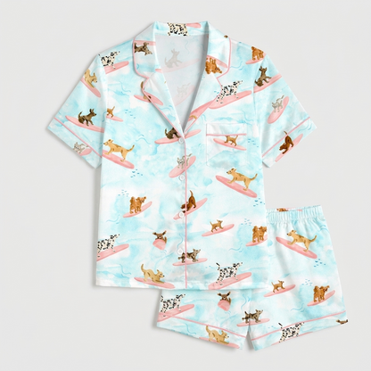 Women's satin pajama set with dalmatians and terriers surfing on pink boards on watercolor blue - flat lay