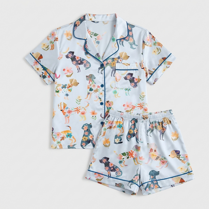 Women's satin pajama set with dog silhouettes filled with orange, pink and navy flowers on white with blue piping - flat lay