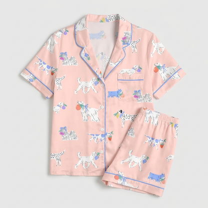 Women's satin pajama set with Dalmatians in periwinkle bows holding tiny bouquets on soft blush pink - flat lay