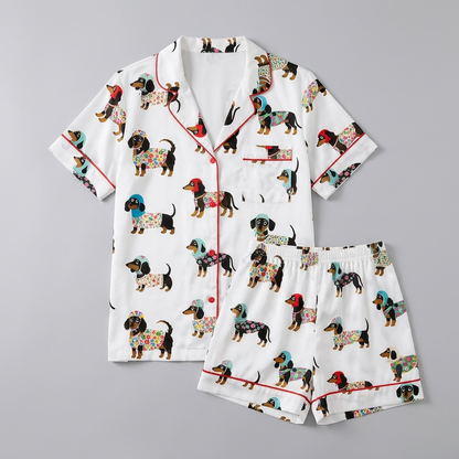 Women's satin pajama set with black-and-tan dachshunds in patterned sweaters and knit hats on white with red piping - flat lay