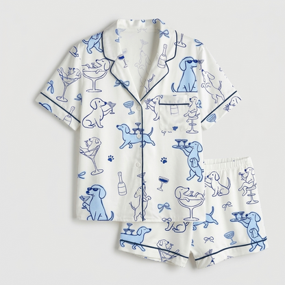 Women's satin pajama set with blue dachshunds in sunglasses toasting with martinis and champagne on white - flat lay