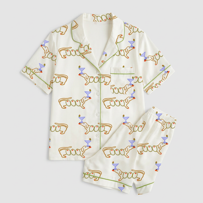 Women's satin pajama set with orange-outlined dachshunds beside lavender martini glasses on white - flat lay