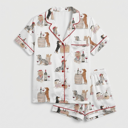 Women's satin pajama set with dachshunds on wine barrels beside bottles and cork-topped crates on white - flat lay