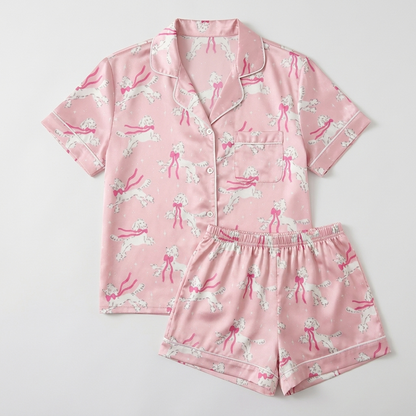 Women's satin pajama set with white poodles trailing hot pink ribbons on soft pink - flat lay