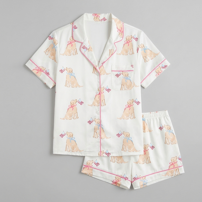 Women's satin pajama set with golden retriever puppies in bows holding tiny flags on soft cream - flat lay