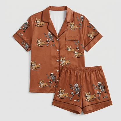 Women's satin pajama set with a skeleton chasing a corgi past a graveyard tree on rust brown - flat lay