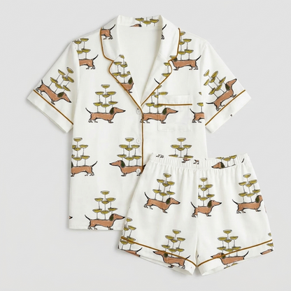 Women's satin pajama set with dachshunds balancing towers of champagne coupes on their backs on white - flat lay