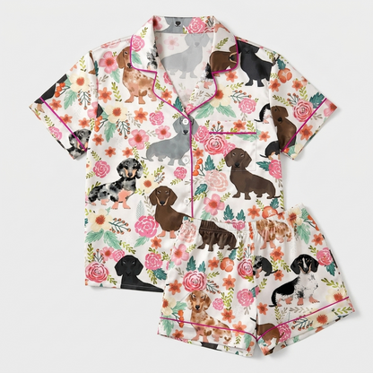Women's satin pajama set with dachshunds among pink roses, peach blooms and leaves on white - flat lay