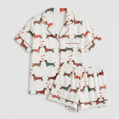 Women's satin pajama set with dachshunds in red, green and teal sweaters among tiny hearts on white - flat lay