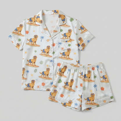 Women's satin pajama set with golden retrievers surfing among palm trees and hibiscus - flat lay