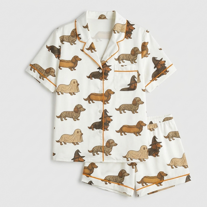 Women's satin pajama set with dachshunds dressed as ghosts, mummies and witches on creamy white with orange piping - flat lay