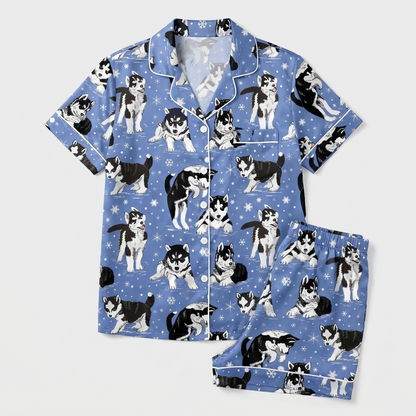 Women's satin pajama set with black-and-white huskies in scarves among snowflakes on periwinkle blue - flat lay