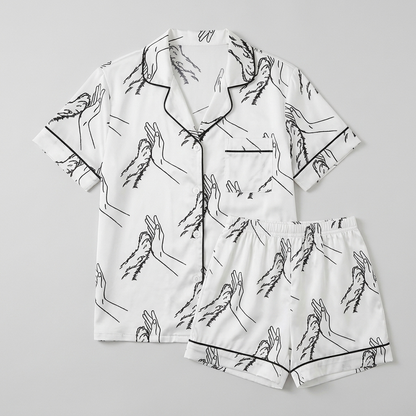 Women's satin pajama set with a black line drawing of a hand high-fiving a dog paw on white - flat lay