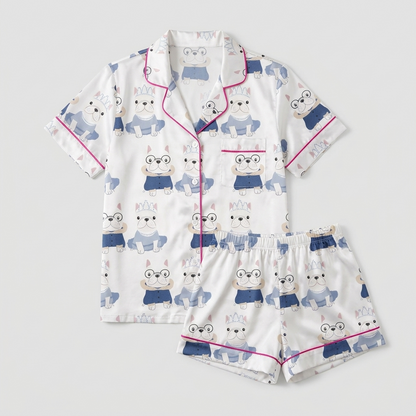 Women's satin pajama set with frenchies in round glasses and navy jackets beside a tiara-wearing pup in a tutu - flat lay