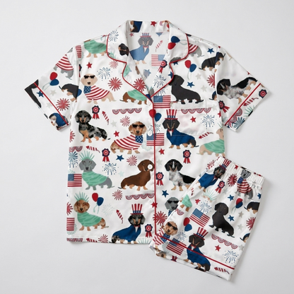 Women's satin pajama set with dachshunds in flag capes and Liberty crowns beside fireworks and stars on white - flat lay