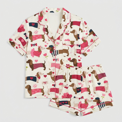 Women's satin pajama set with dachshunds in pink and red sweaters among hearts and balloons on white - flat lay