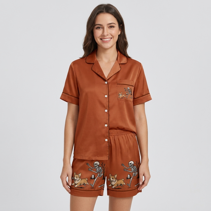 Women's satin pajama set with a skeleton chasing a corgi past a graveyard tree on rust brown - short sleeve and shorts