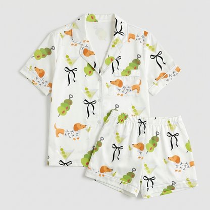 Women's satin pajama set with orange dachshunds, martinis, olive skewers and black bows on white - flat lay