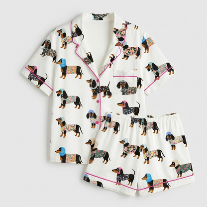 Women's satin pajama set with black-and-tan dachshunds in floral coats and knit hats on white - flat lay