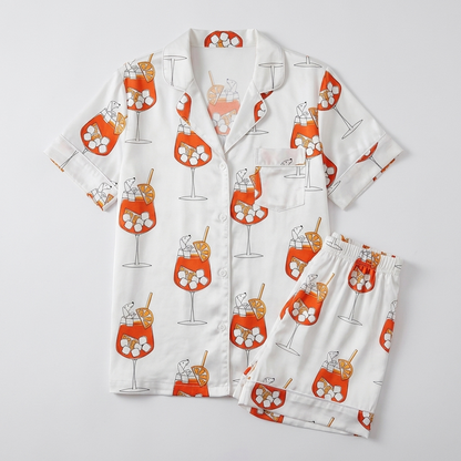 Women's satin pajama set with dachshunds tucked into orange spritz glasses on crisp white - flat lay