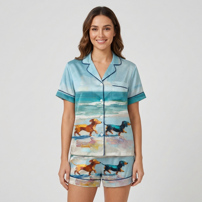 Women's satin pajama set in sky blue with a red and a black dachshund racing along an oil-painted shoreline - short sleeve and shorts